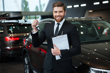 Handsome young car salesman standing at the dealership