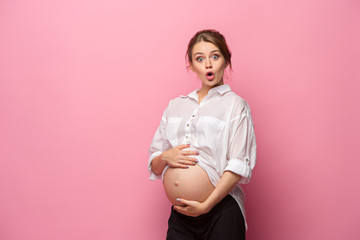 Young beautiful pregnant woman standing on pink background