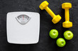 Sport and diet for losing weight. Bathroom scale, apple and dumbbell on black background top view