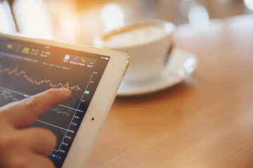 Business Hand Analyzing Stock finance Graph on Tablet with Coffee on wood background