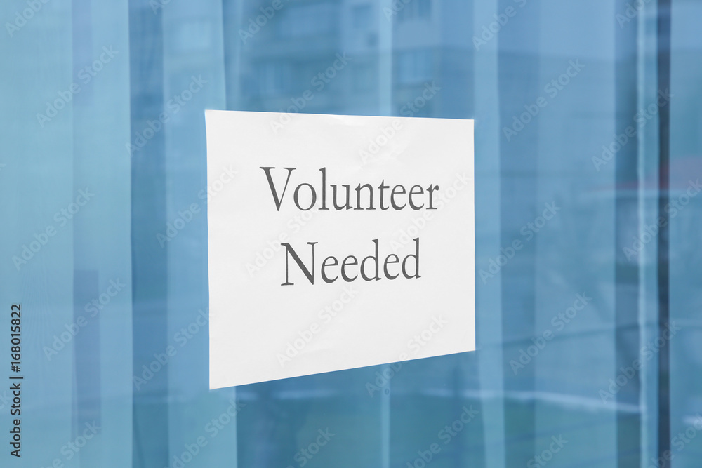 Sheet of paper with text VOLUNTEER NEEDED on window glass