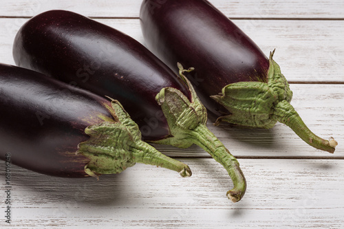 Three fresh eggplants on a white wooden surface. Poster
