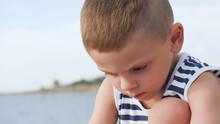 Little Boy Pulls Out The Splinter And Finger Sitting On The Beach Close Up