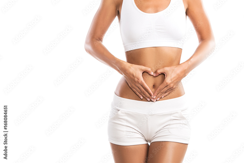 Fit young woman holding a heart over her abdomen, isolated on white background - obrazy, fototapety, plakaty 