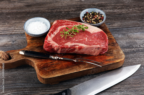 Fotografía Carne cruda fresca Ribeye Steak, condimentos y tenedor de carne sobre fondo oscu