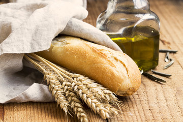 Baguette bread in linen towel with olive oil and ears of wheat