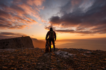 Silhouette of young man with his dog at dawn with sea and mountain on background.