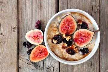 Wall Mural - oatmeal with red figs, cranberries and walnuts in a bowl, above view on rustic wood