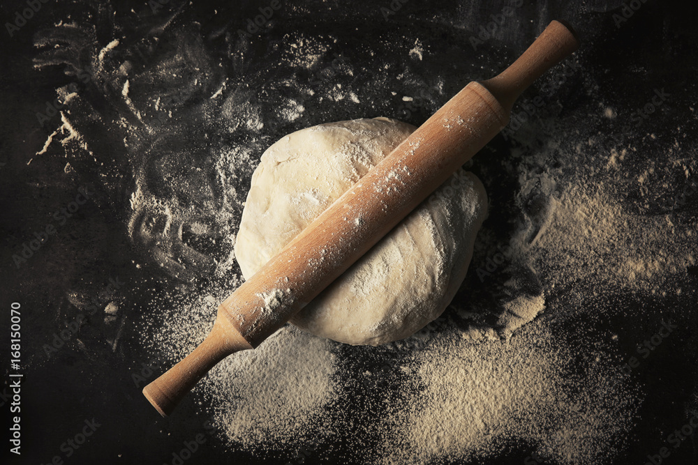 Raw dough and rolling pin on dark table