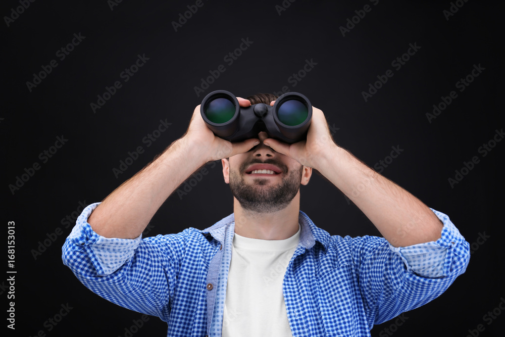 Handsome young man with binocular on dark background