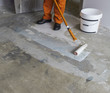 Worker puts primer with roller on concrete floor in room of unfi