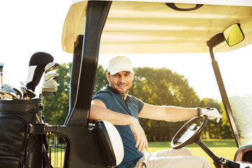 Smiling young male golfer sitting in a golf cart