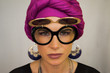 © Artem Markin - A beautiful European woman in a bright pink turban with large oriental earrings, in large round glasses looks at the camera. The style of urban fashion.