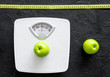 © 9dreamstudio - Lose weight concept. Bathroom scale, measuring tape, apples on black background top view