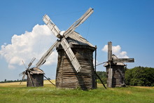 Three Wooden Log Windmills In The Field At Sunny Day