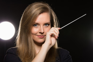 Wall Mural - Young caucasian woman conductor poses with baton in a dark space with stage lights