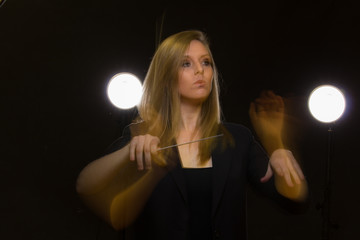 Wall Mural - Young caucasian woman conductor gestures with baton and leaves light trails