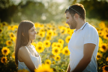 Wall Mural - A sweet woman in love looks at her husband, who holds the lady by the hands in the field of the halfpings, the couple is spending a romantic date in nature on a warm summer day