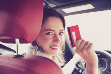 Happy young woman sitting inside her new car showing credit card