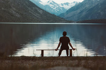 A Lonely Man Sitting On The Bench In Front Of The Lake