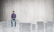 © adam121 - Attractive man sitting on pile of paper documents.
