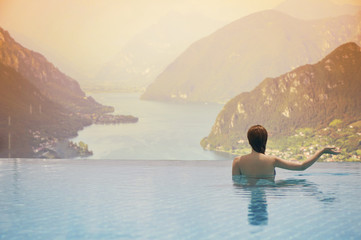 Young female in the pool on the roof in the background of Italian mountain and clouds in South Tyrol. Female in the swimming pool on the roof opposite lake and mountain