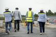 © bannafarsai - Group of workmen wearing protective helmets and vests walking among concrete walls of unfinished building showing development progress to foreman inspector on construction site