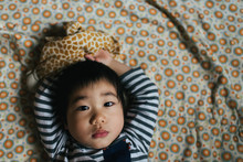 Asian American Toddler Boy Laying On Blanket With Arms Over Head