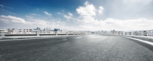 Empty Road And Cityscape Of Modern City Against Cloud Sky