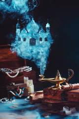 Magic lamp with mystic smoke forming an arabic castle, still life with treasure and jewelry.