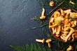 Yellow mushrooms chanterelle (cantharellus cibarius) in vintage plate with forest plants on dark kitchen table top view. Copy space for text.