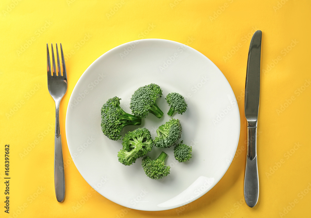 Plate with fresh broccoli on yellow background