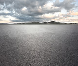 Fototapeta Koty - Asphalt road with cloudy sky and mountain background