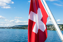 Swiss National Flag On Lake With Water And Blue Sky