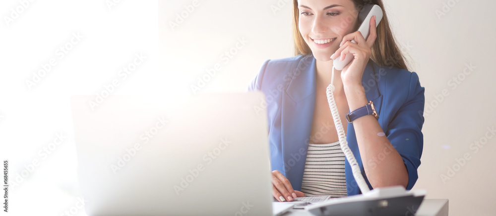 Portrait of a young woman on phone in front of a laptop computer - obrazy, fototapety, plakaty 