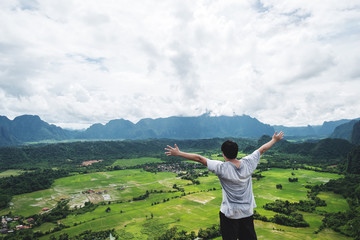Wall Mural - a man raising hand up on mountain peak, traveling in tropical countryside, vang vieng in laos