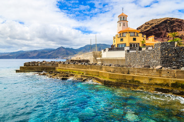 Emerald green ocean water and lighthouse building on coast of Madeira island, Portugal