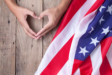 Gesture Made By Hands Showing Symbol Of Heart With American Flag On Old Wooden Background.