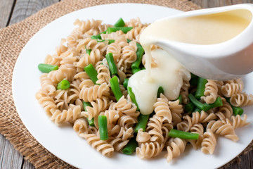 Pouring white sauce over plate of cooked pasta