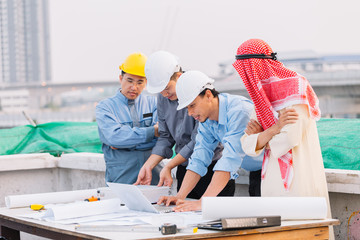 Wall Mural - Arabian businessman and Engineer and Laborer working and discussion with laptop  on construction plans front of building in his work site. Teamwork concept