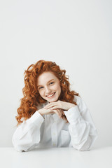 Wall Mural - Beautiful redhead girl with curly hair smiling looking at camera sitting at table over white background.