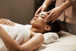 © Cookie Studio - Attractive african girl enjoying face massage in spa salon.
