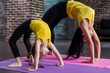 © undrey - Kids yoga female teacher training a child girl standing in wheel pose working out in stylish sports studio