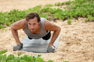 Fitness man doing plank push-ups exercise on dumbbell weights on beach. Bodyweight floor exercises healthy lifestyle.