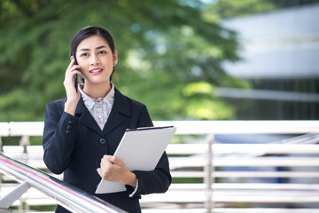 Young Beautiful business woman in city using smartphone for work. Young Business Woman Workwith Smartphone  Concept. Asian Woman Talking for Business Project with Partner.