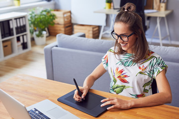 Wall Mural - Cheerful young female graphic designer smiling while working in her office