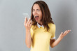 Angry furious girl yelling at mobile phone while standing