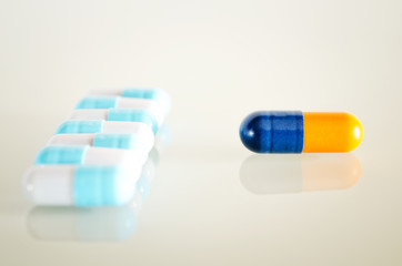 Wall Mural - Two black isolated medical capsule lies on the white mirror surface, in front of the multicolored capsules. Closeup