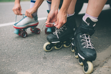 Two slim and sexy young women and roller skates. One female has an inline skates and the other has a quad skates. Girls ride in the rays of the sun