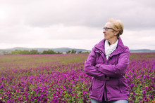 Older Woman Standing At Field Of Purple Flowers And Enjoying The View